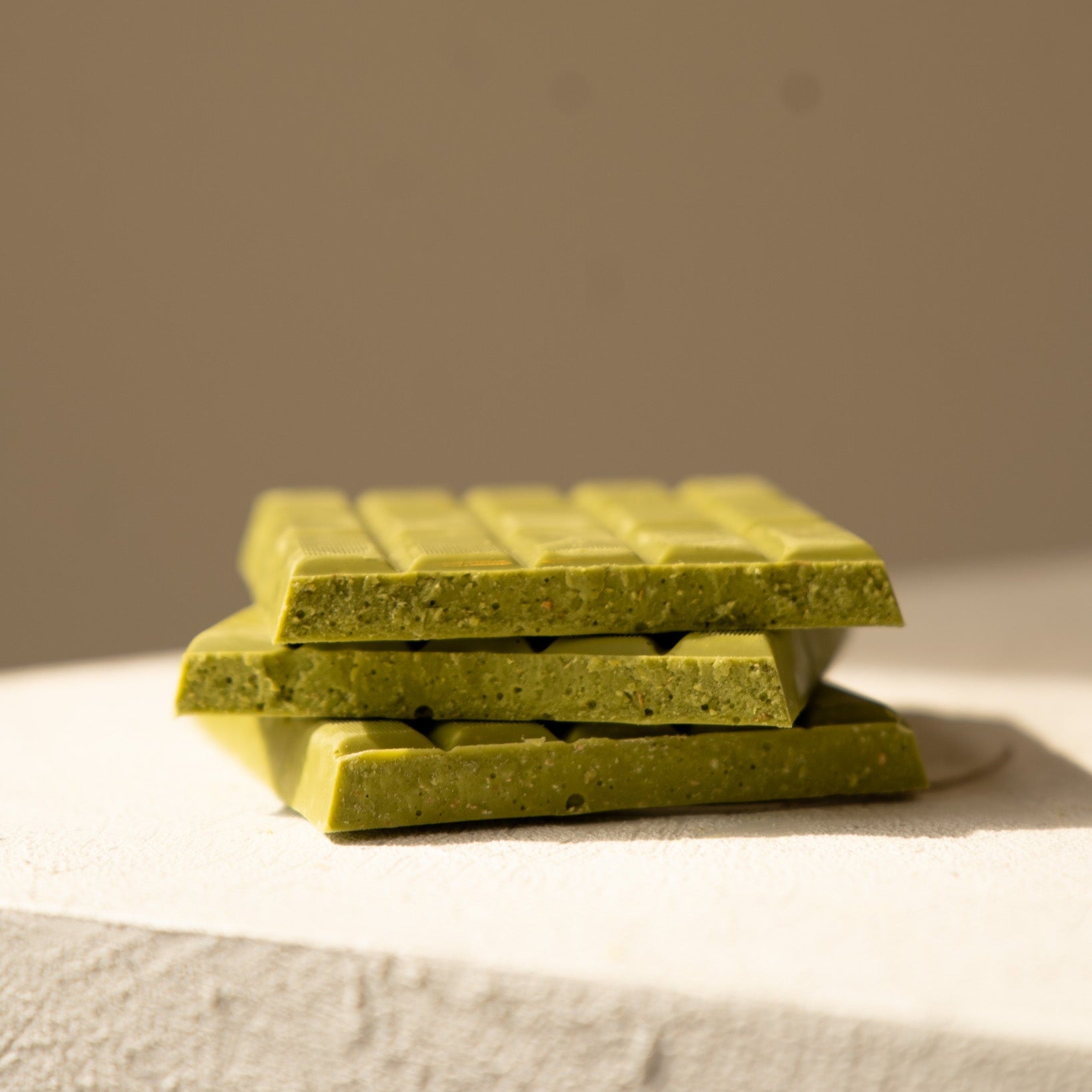 Stack of green chocolate bars on a textured surface with a neutral background