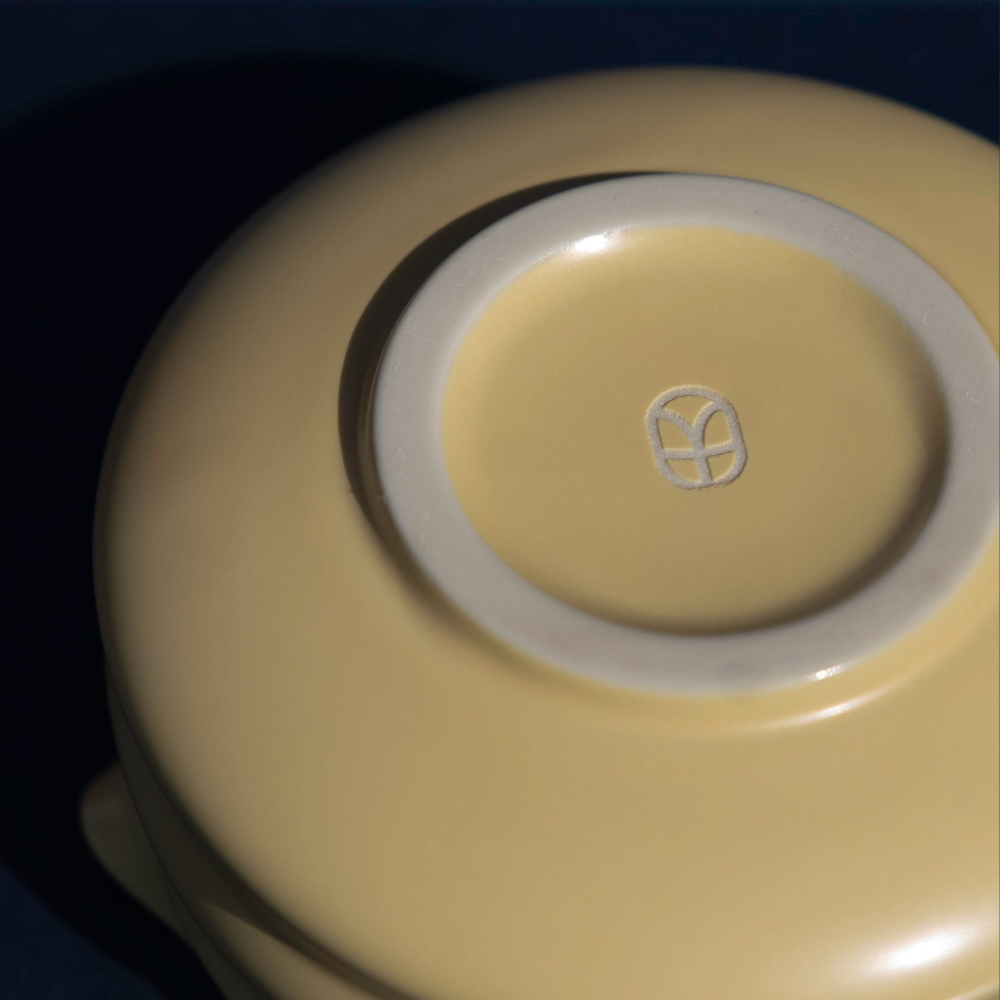 Close-up of a yellow ceramic dish with a logo on a dark background